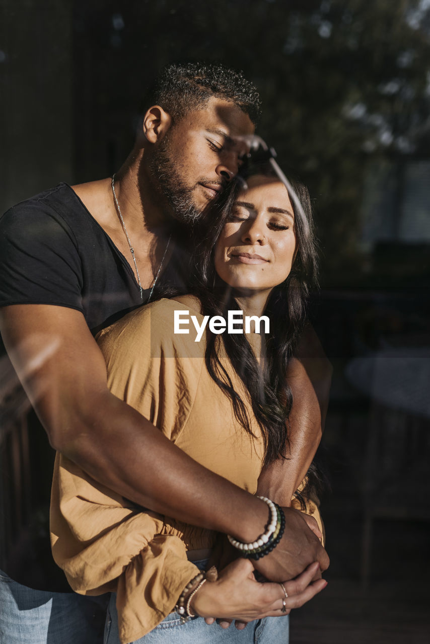 Man embracing woman standing with eyed closed at home