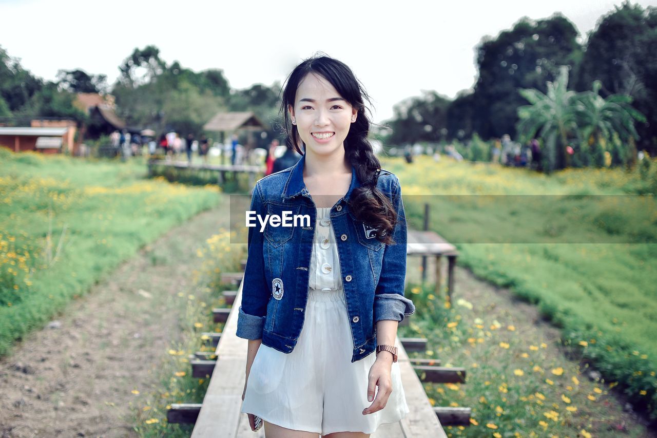 PORTRAIT OF SMILING WOMAN STANDING OUTDOORS