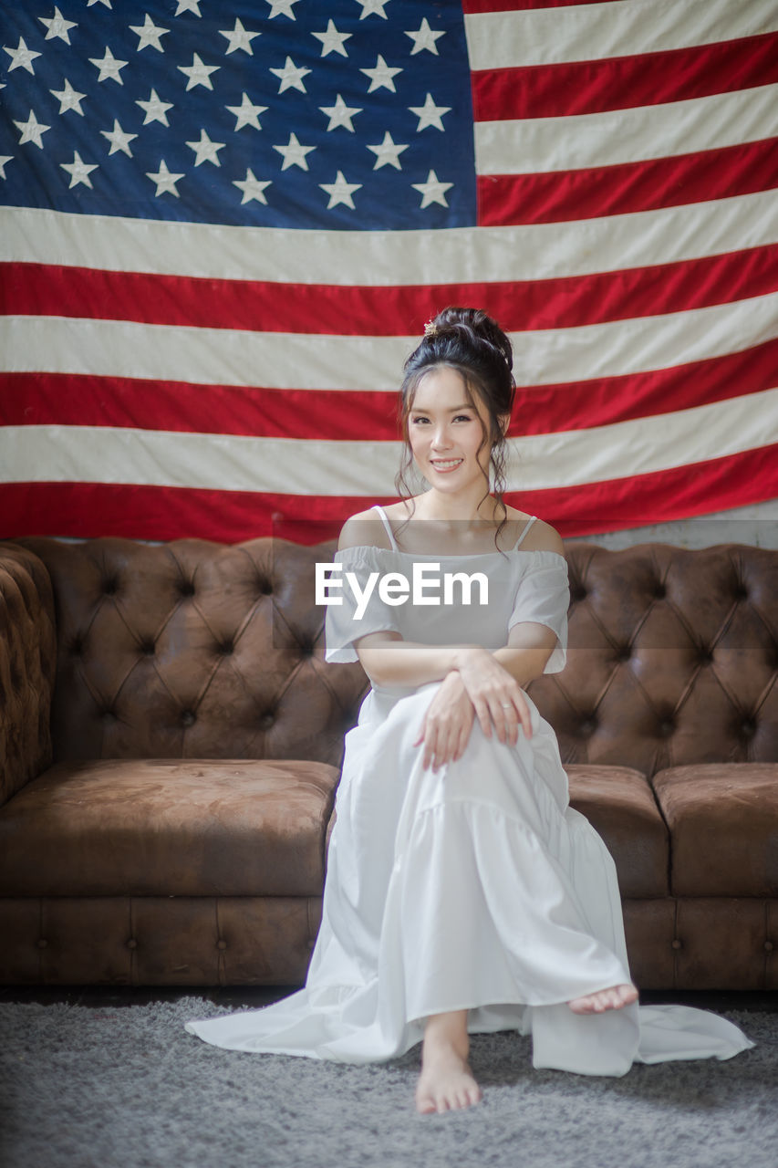 Portrait of smiling young woman sitting on sofa against american flag