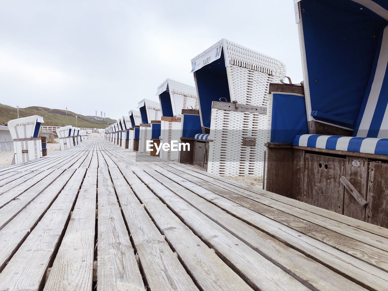 Footpath made of wooden planks on the beach through deck chairs against sky
