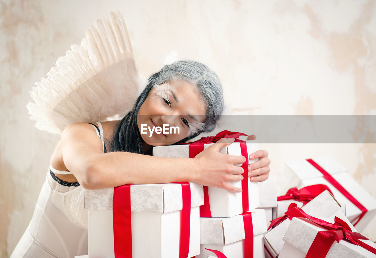 Portrait of female model in angel costume holding christmas presents