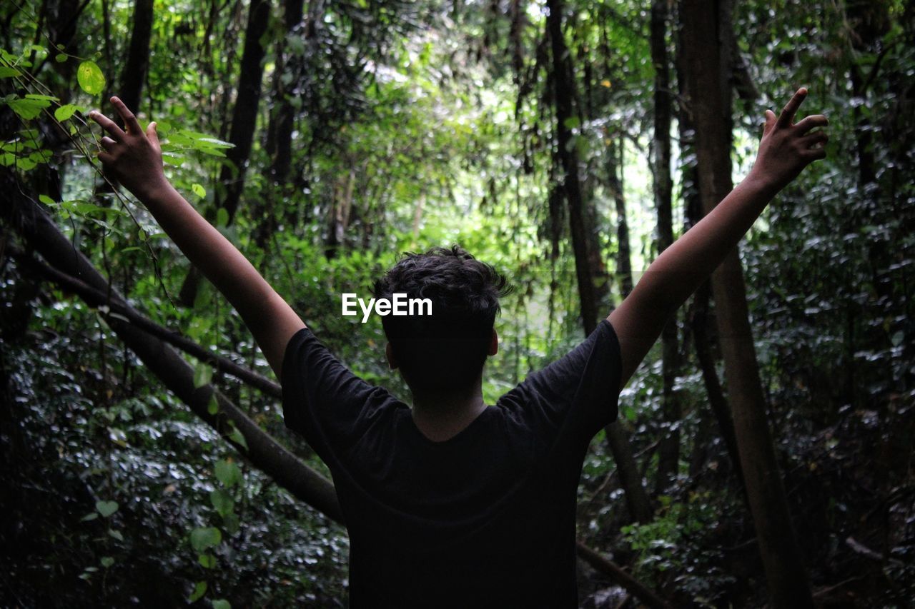 Rear view of teenage boy with arms outstretched standing in forest