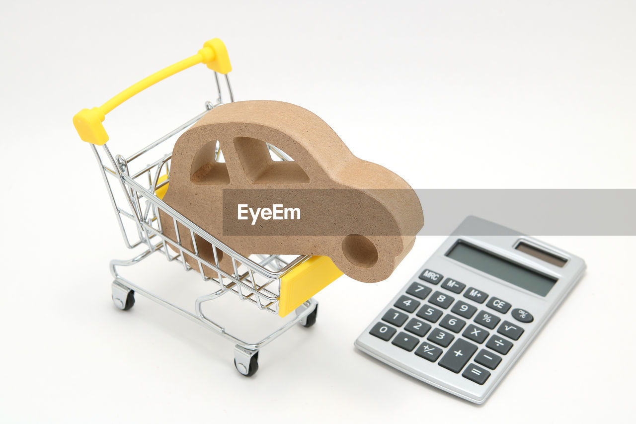 High angle view of car figurine in shopping cart with calculator against gray background
