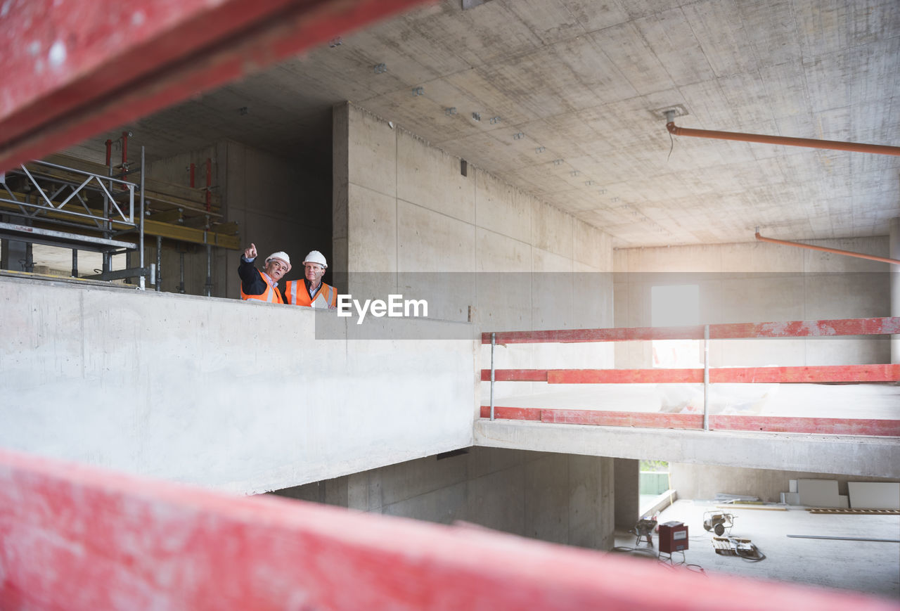 Two men wearing safety vests talking in building under construction