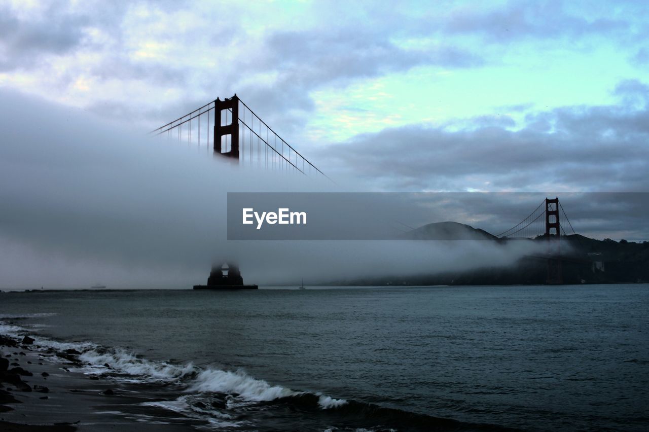 Golden gate bridge covered in fog over bay against sky