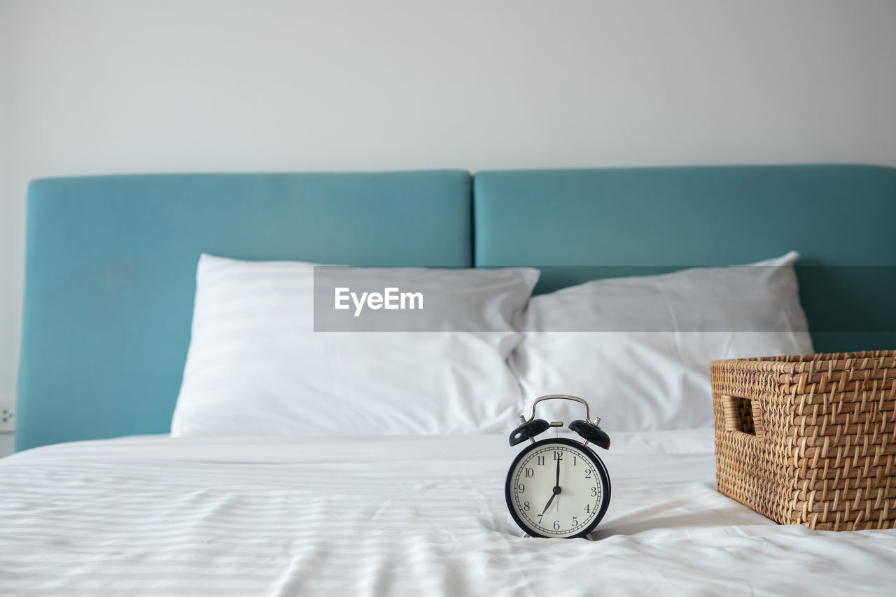 Clock by wicker basket on bed at home