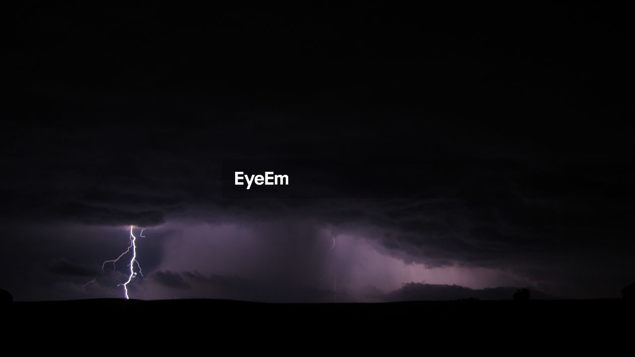 LOW ANGLE VIEW OF LIGHTNING OVER SILHOUETTE LANDSCAPE