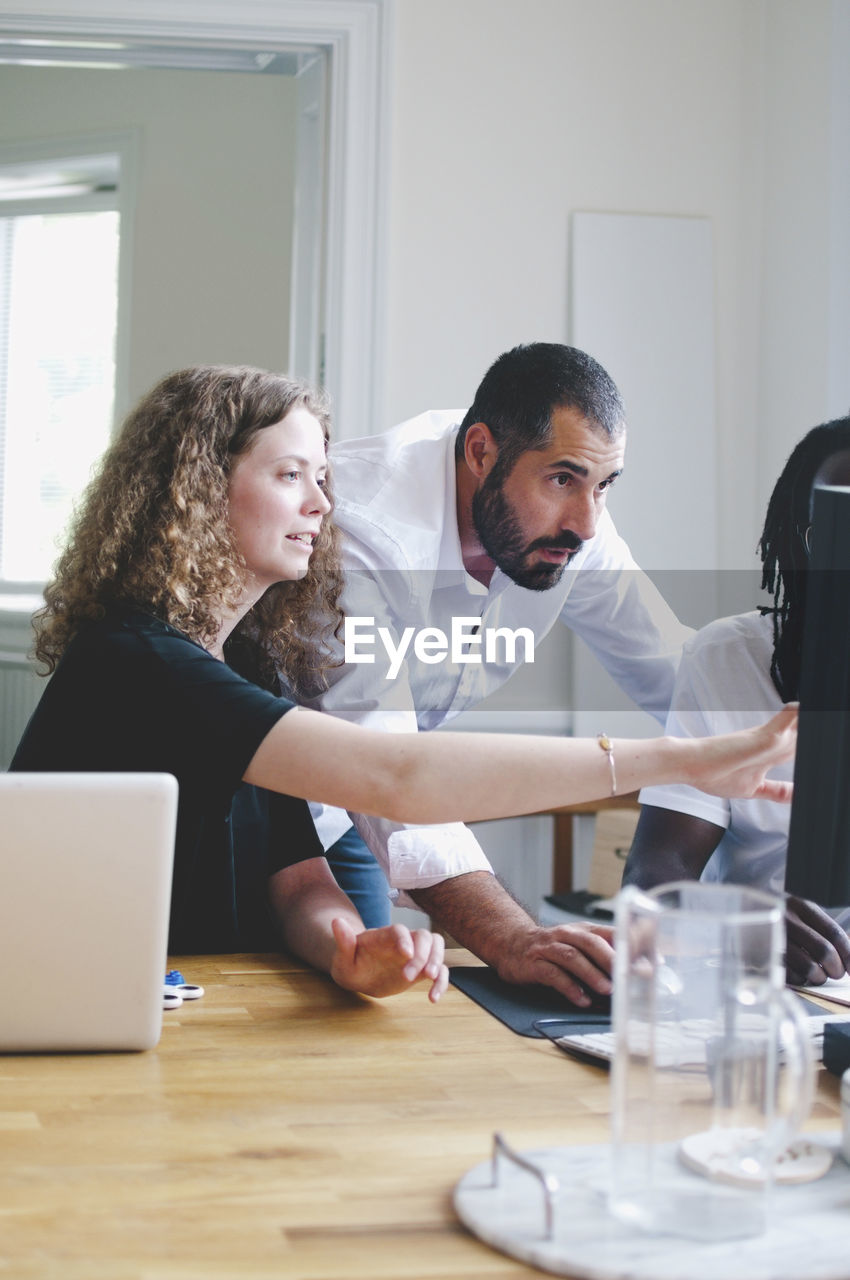 Businesswoman discussing with colleagues over computer in creative office