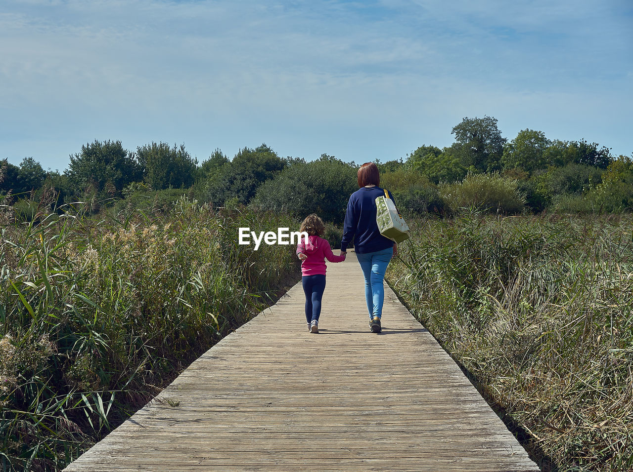 Rear view of woman with daughter walking on boardwalk amidst plants