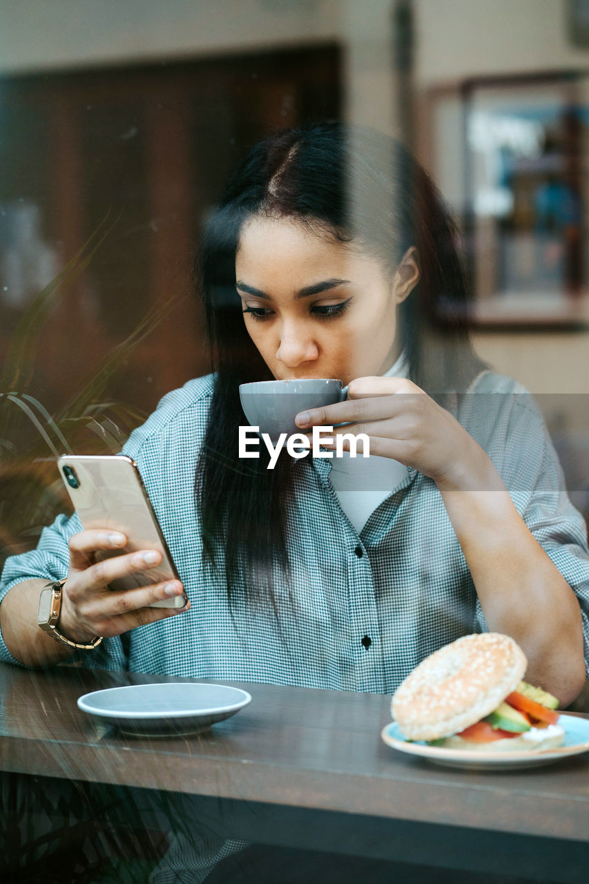 Woman drinking a cup of coffee and using mobile