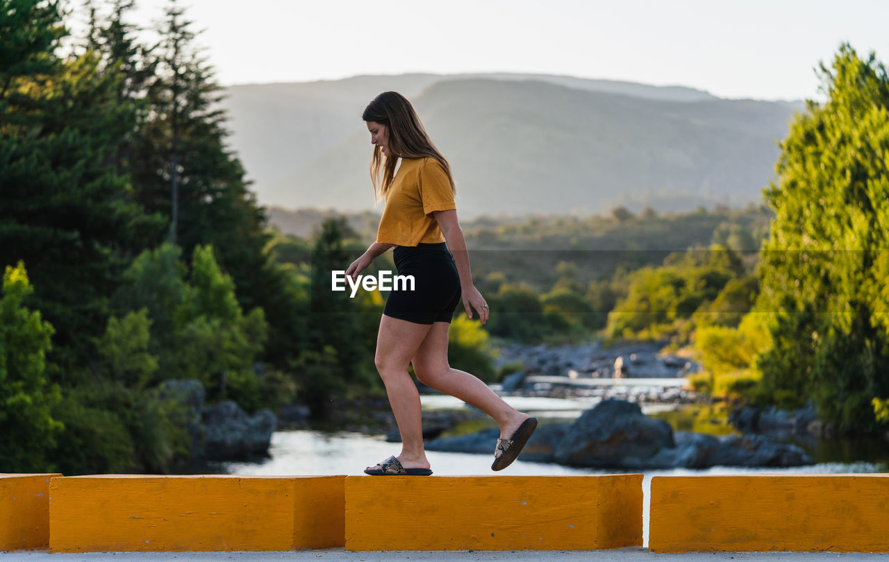 FULL LENGTH OF WOMAN WITH ARMS RAISED ON MOUNTAIN