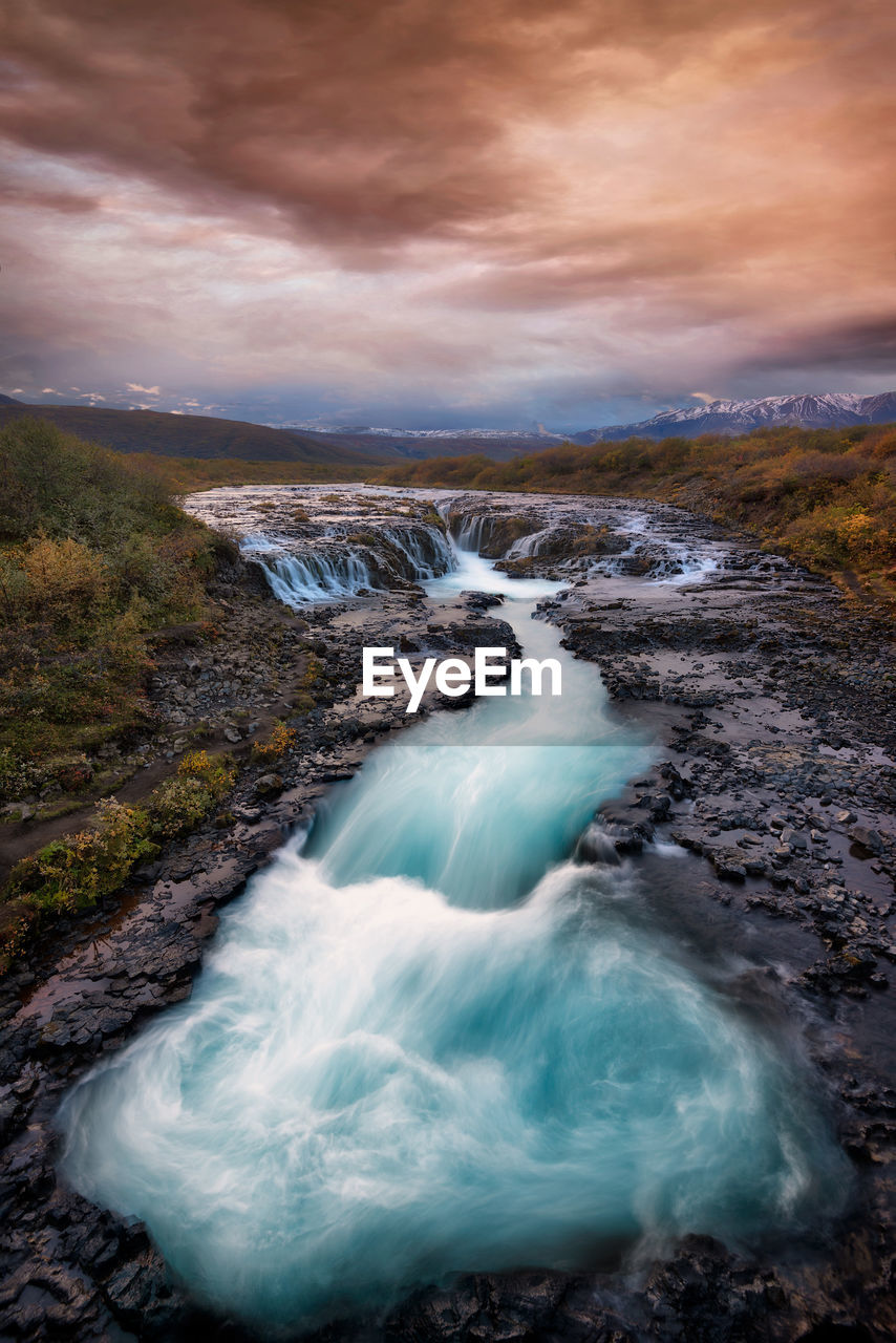 Scenic view of waterfall against sky during sunset