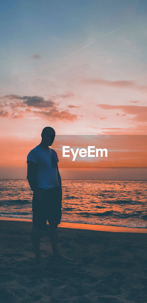 Man standing on sand at beach against sky during sunset