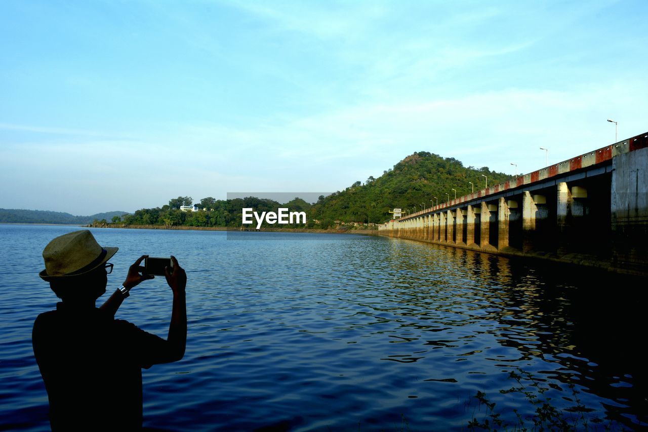 Silhouette man photographing masanjor dam through mobile phone