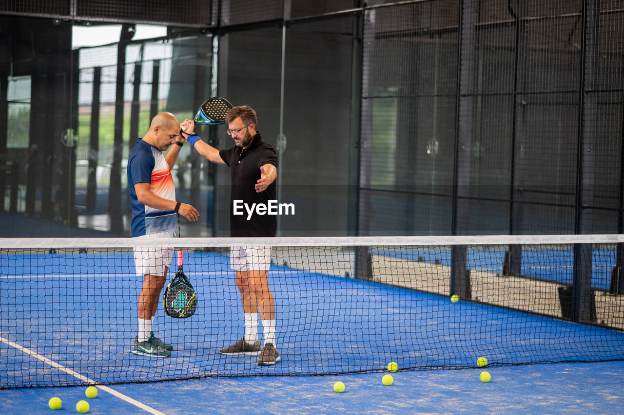 Monitor teaching padel class to man, his student - trainer teaches boy how to play paddle tennis