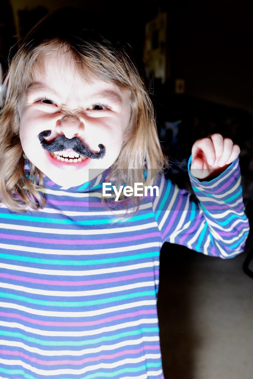 Portrait of cute girl wearing artificial mustache at home