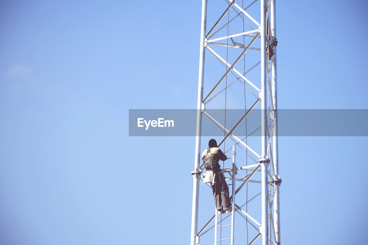 Rear view of worker on pole against blue sky
