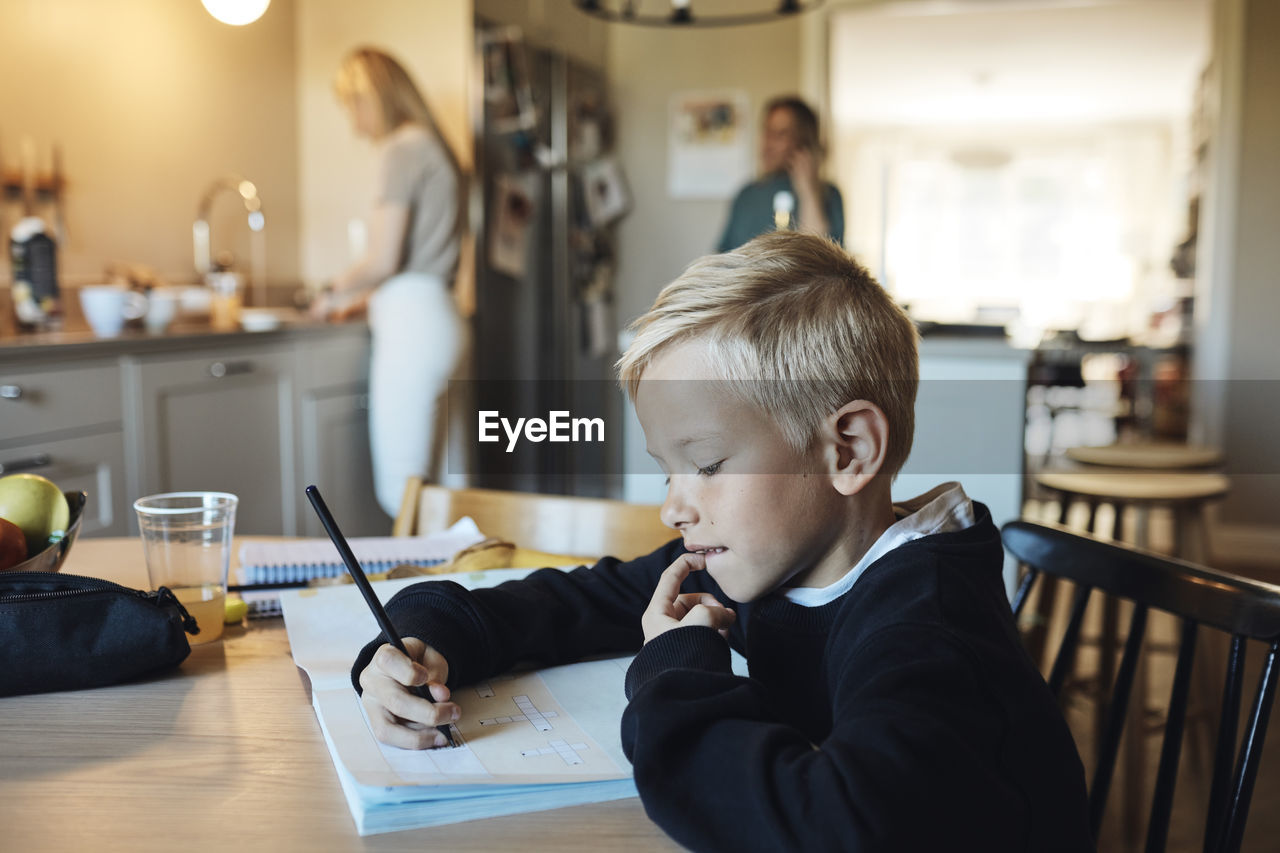 Thoughtful boy doing homework in book while sitting at table