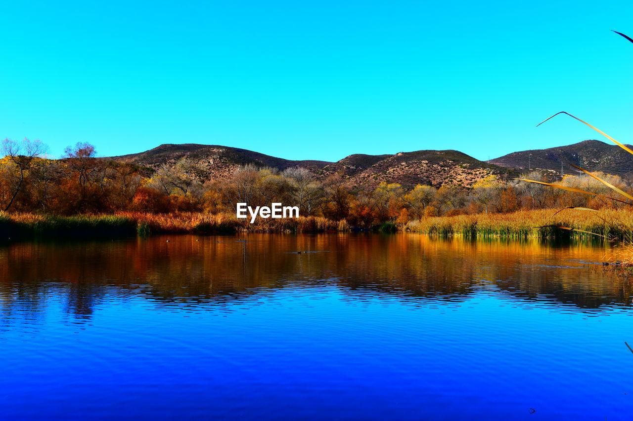 Scenic view of lake and mountains against clear blue sky