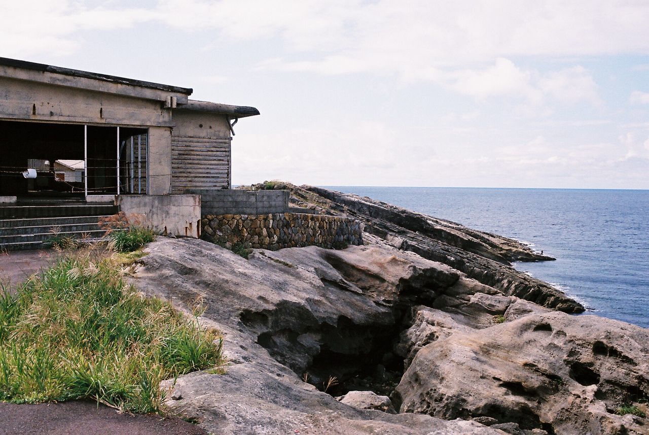 House by rock formations and sea against sky