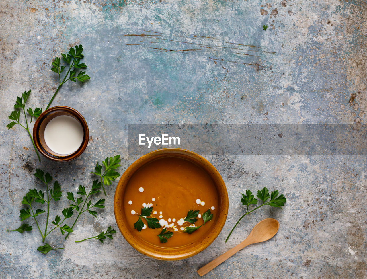 Flat lay idea of hokkaido creamy pumpkin soup and parsley with wooden spoon on a concrete background