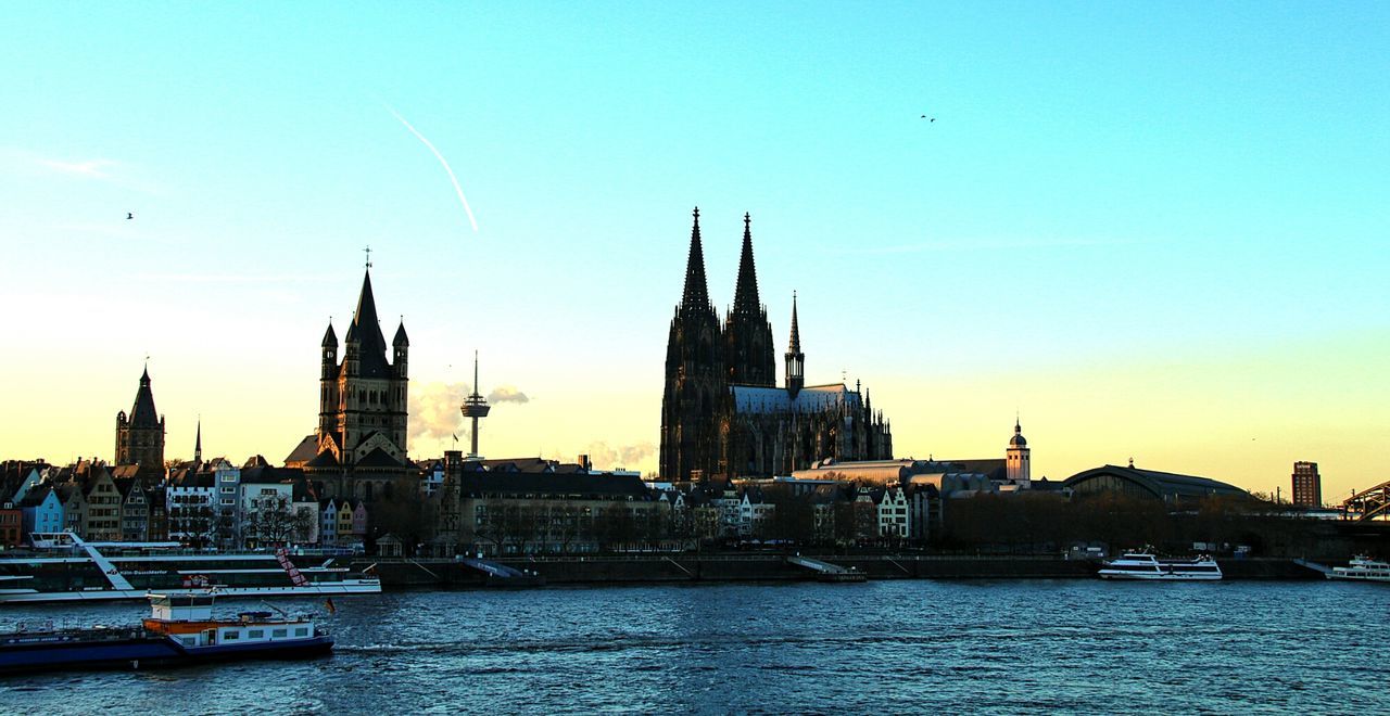 Cologne cathedral by rhine river against sky during sunset