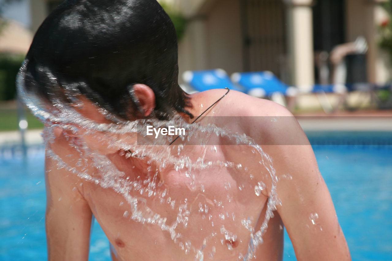 Close-up of boy shaking wet hair by swimming pool