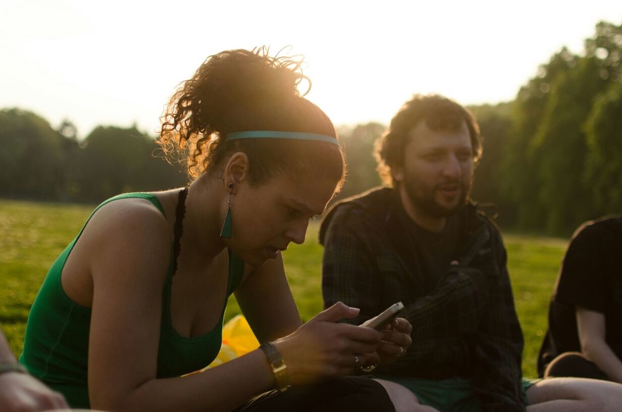 Side view of young woman text messaging with friends on grassland