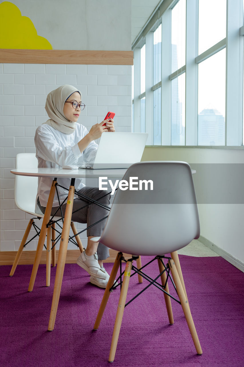 Moslem women using her laptop and smartphone while sitting on chair at table