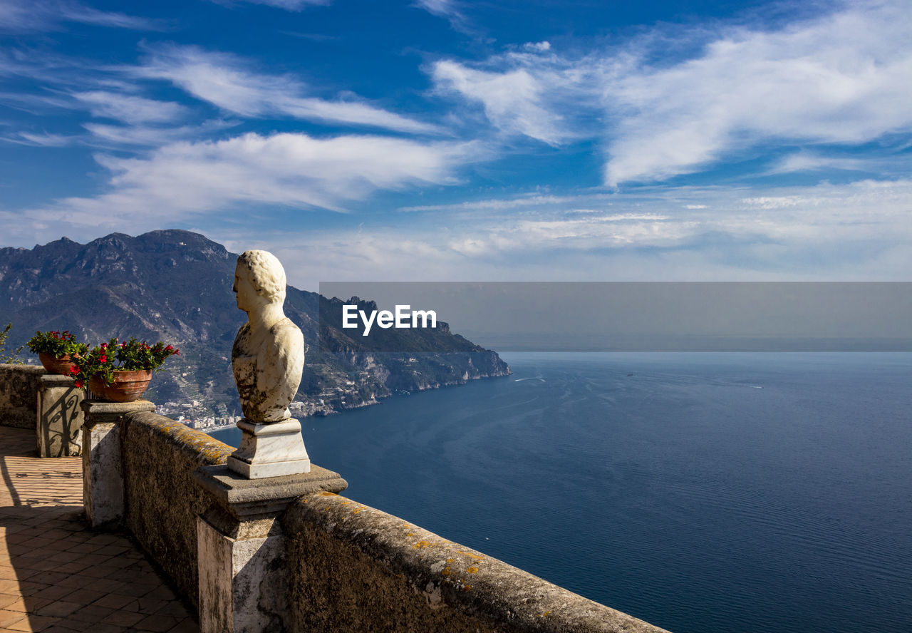 STATUE BY SEA AGAINST MOUNTAIN