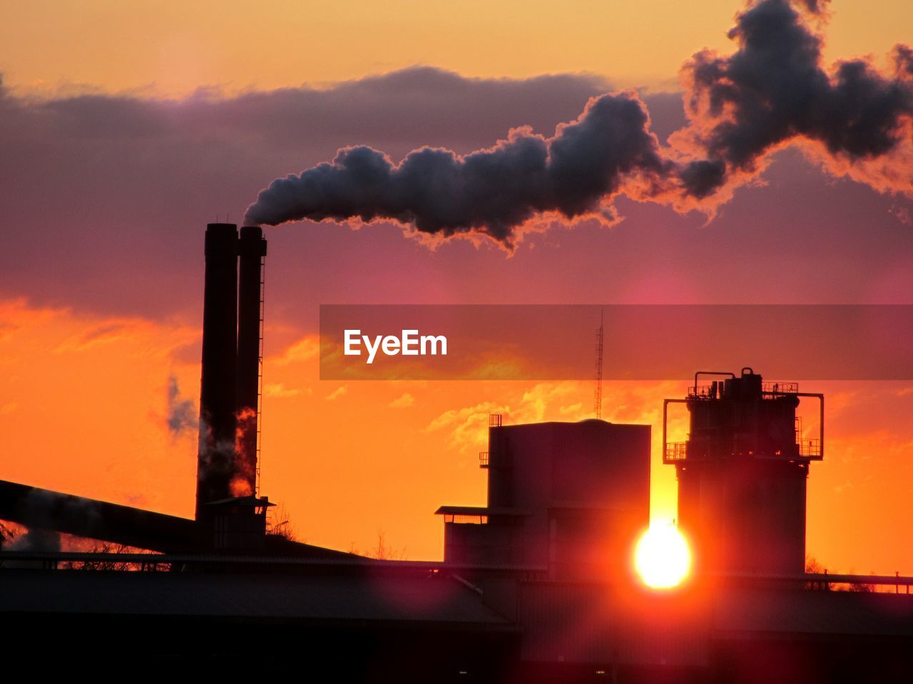 Silhouette smoke stacks against sky during sunset