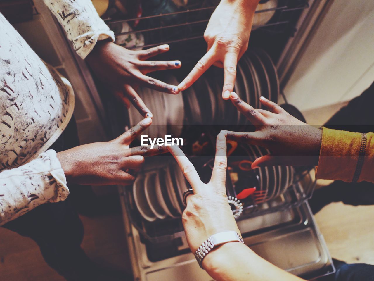 Cropped image of friends making star shape over dishwasher in kitchen