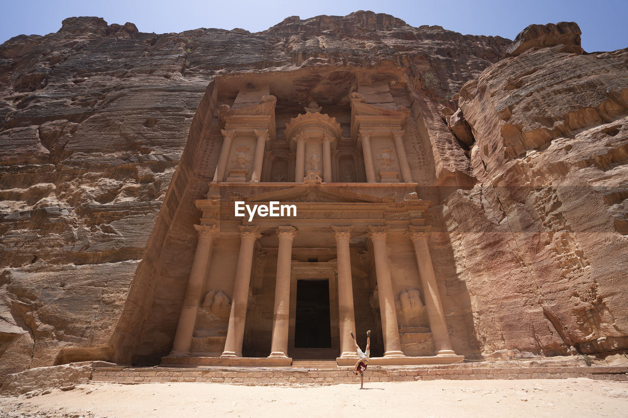 A man does a hand stand near treasury monument in petra, jordan seven wonders