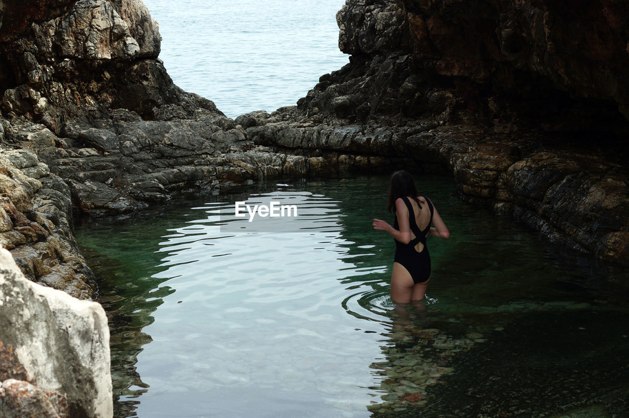 Rear view of woman standing against sea in pond