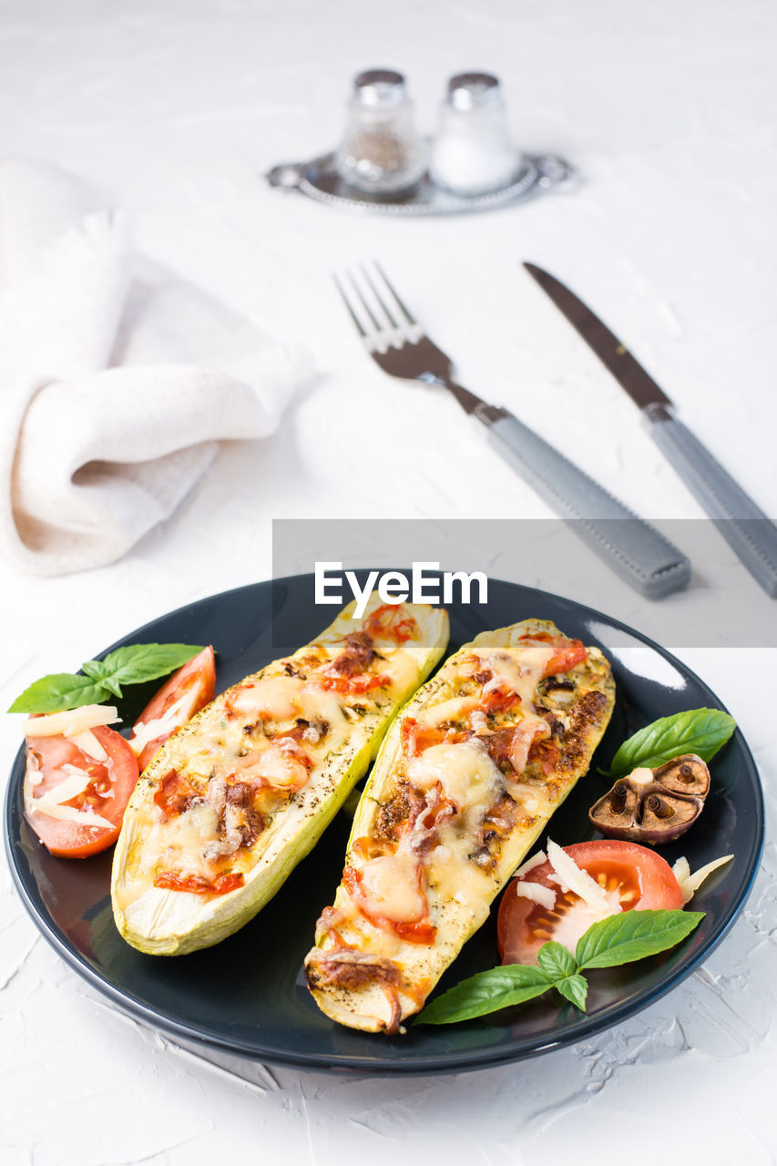 Ready-to-eat baked zucchini halves filled with cheese and tomato and basil leaves and cutlery