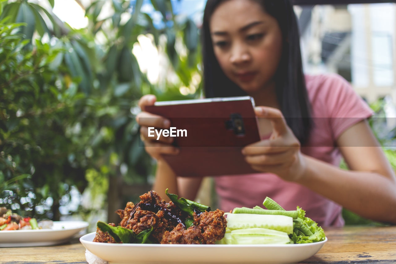 MIDSECTION OF WOMAN HOLDING MOBILE PHONE WHILE TABLE