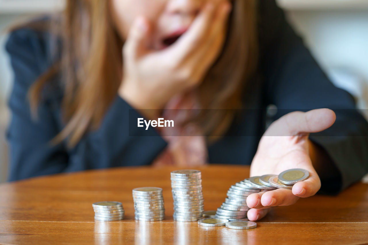 Midsection of shocked businesswoman holding coins at table