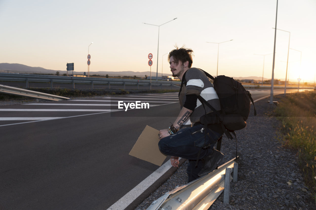 Side view of man standing by road against sky