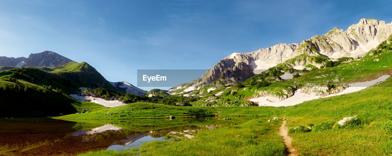 Tent camp on the green flowering shore of a mountain lake surrounded by mountain peaks. adygea