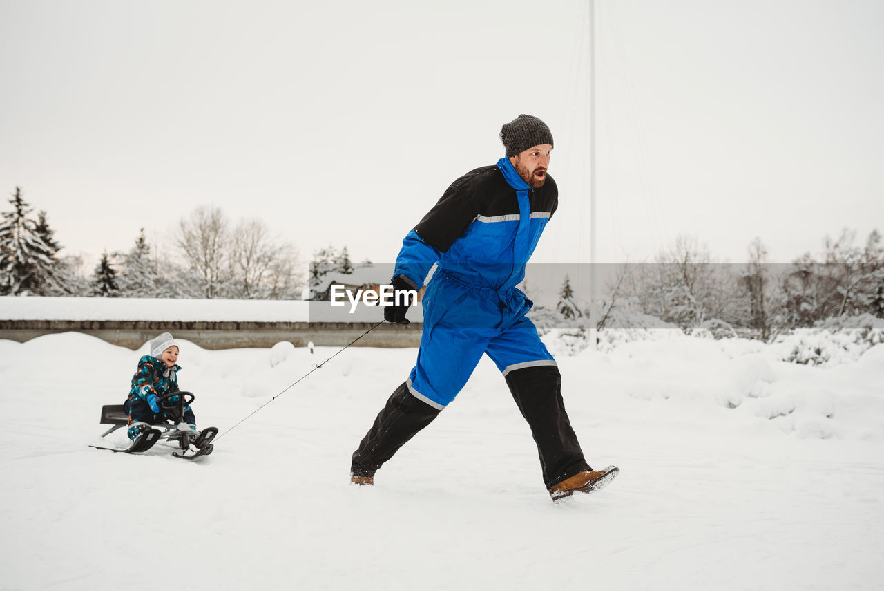 Fun dad pulling sleigh where son is sitting on in winter snowy woods