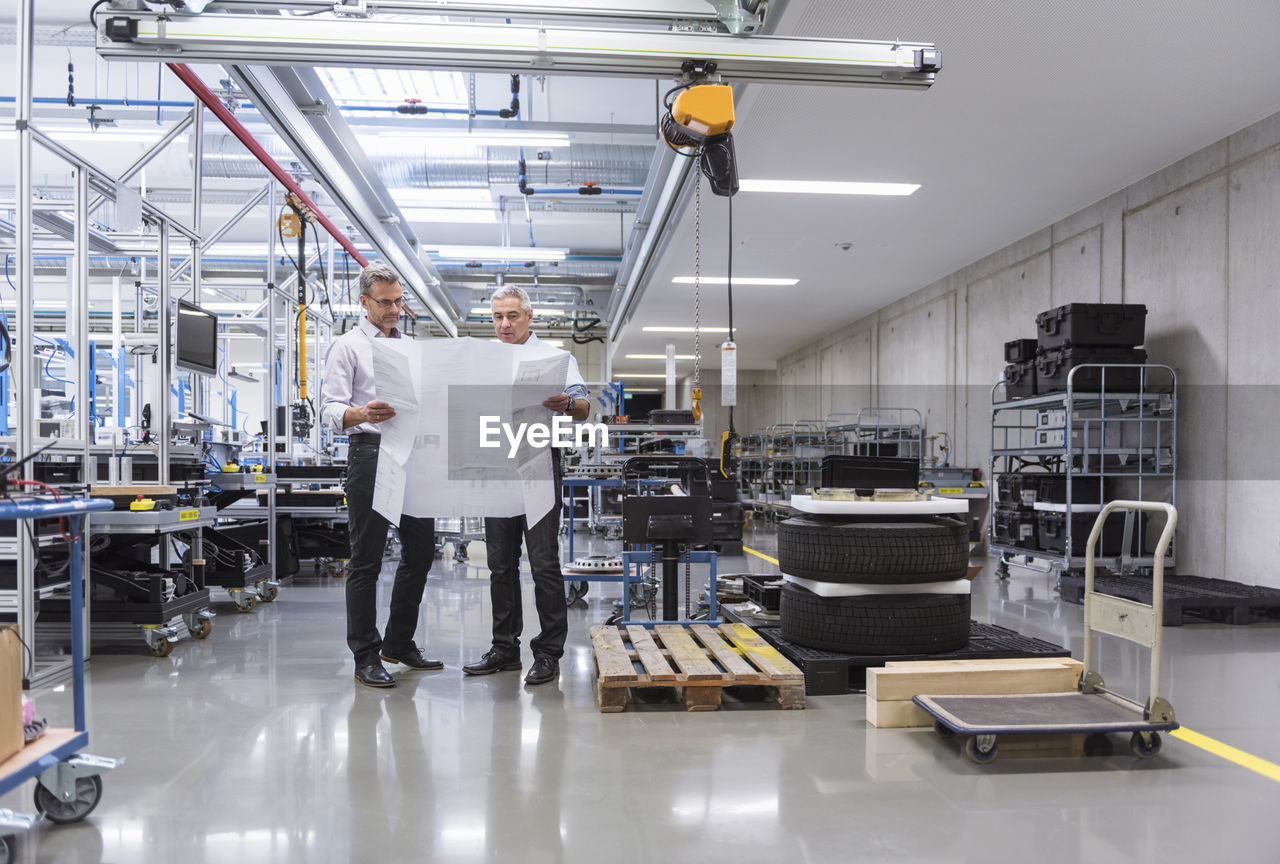 Two businessmen in factory hall discussing construction plan