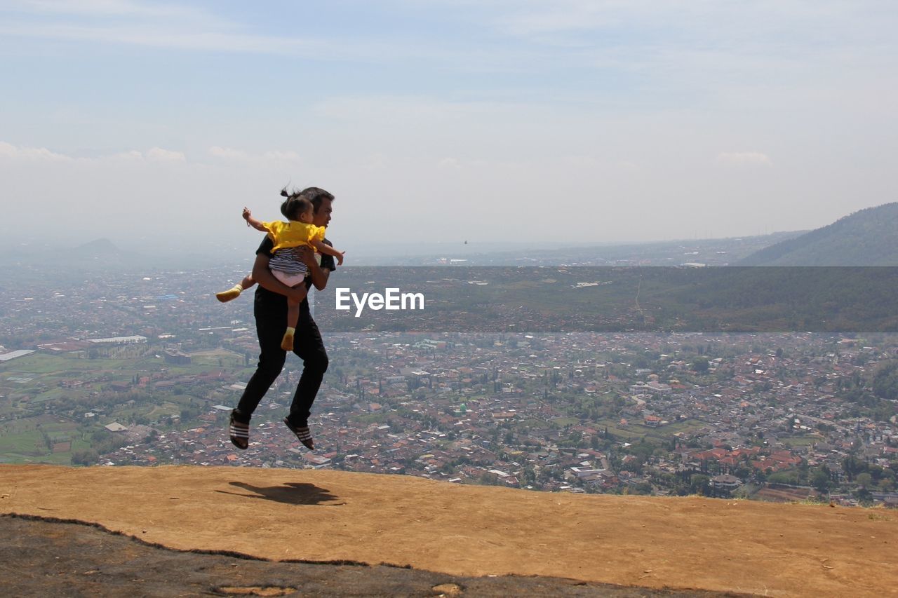 Full length of father with daughter levitating over landscape against sky