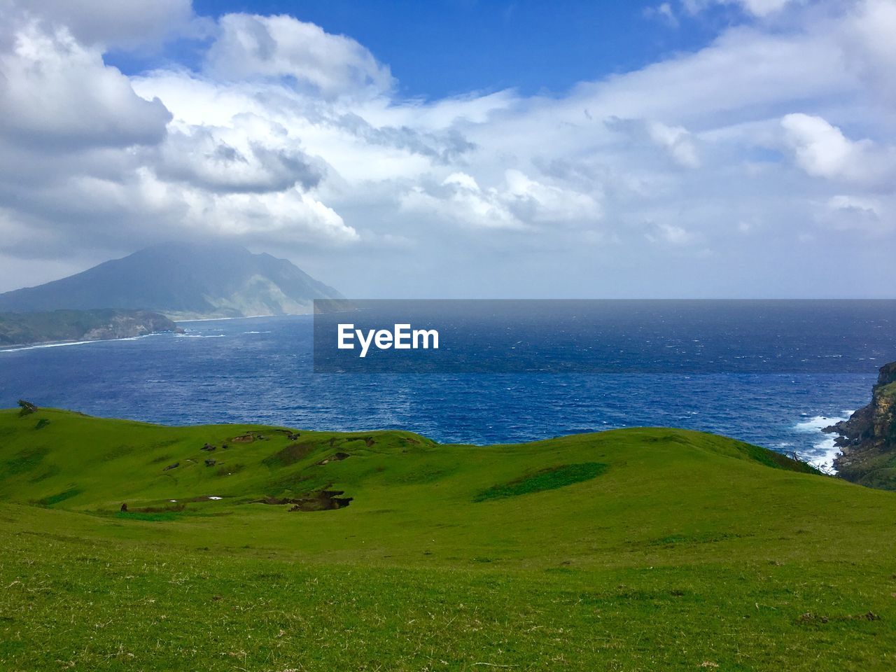 Scenic view of grassy field by sea against cloudy sky 