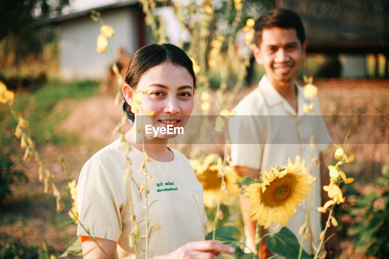 PORTRAIT OF A SMILING GIRL STANDING AGAINST PLANTS