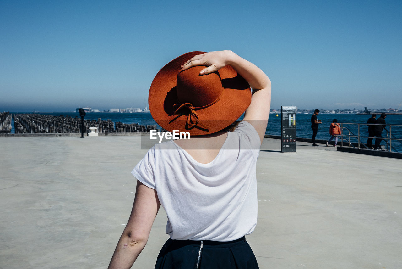 Rear view of woman walking on pier at sea against sky