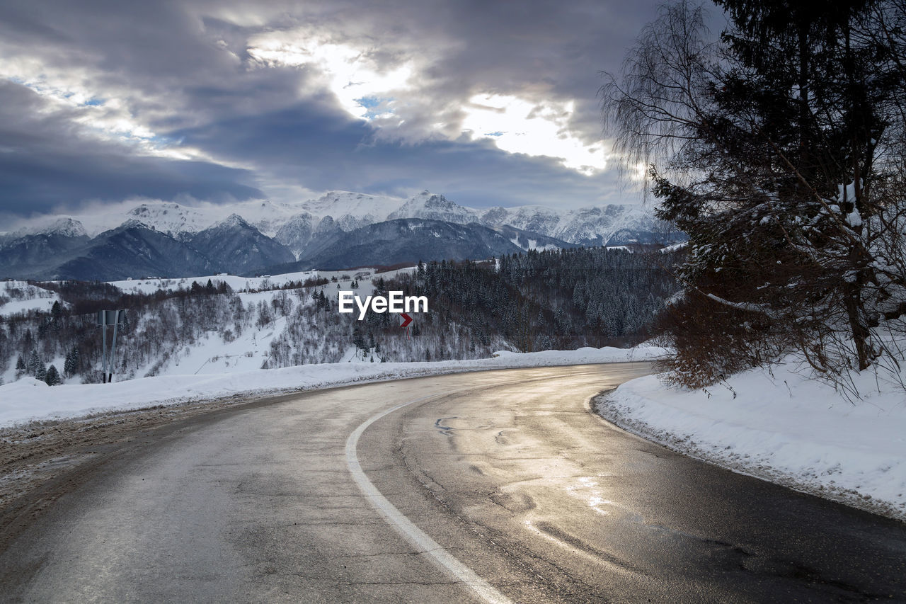 Road by snow covered mountains against sky