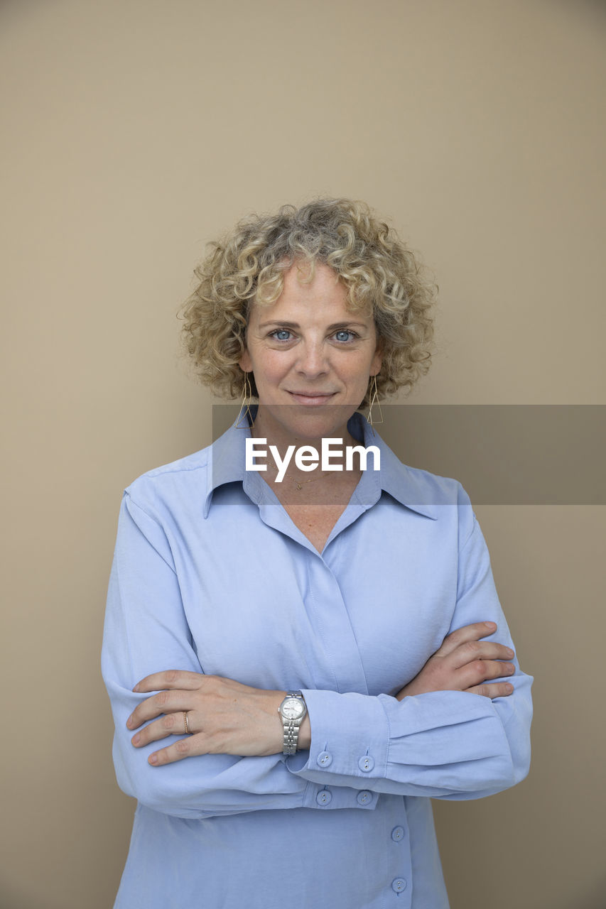 Businesswoman with arms crossed against brown background