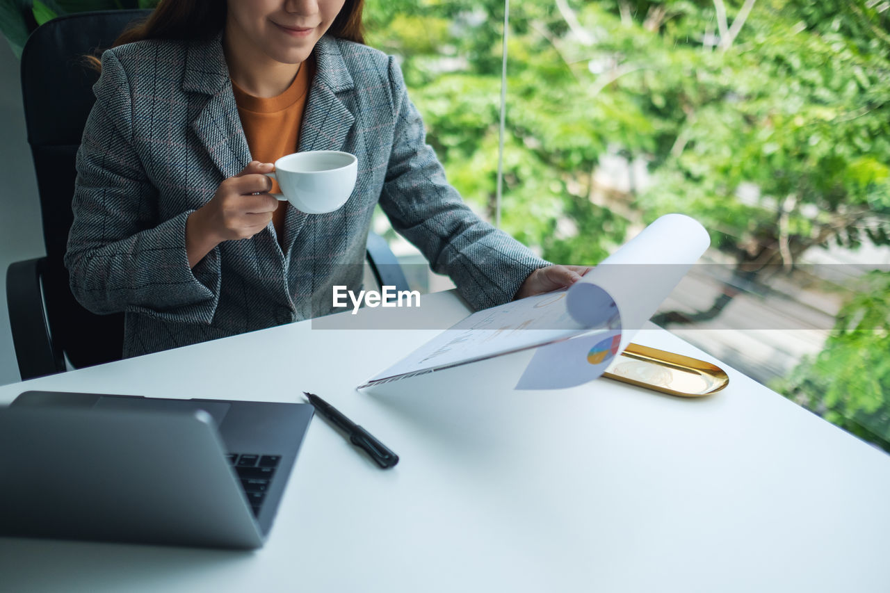 midsection of man using digital tablet while sitting on table