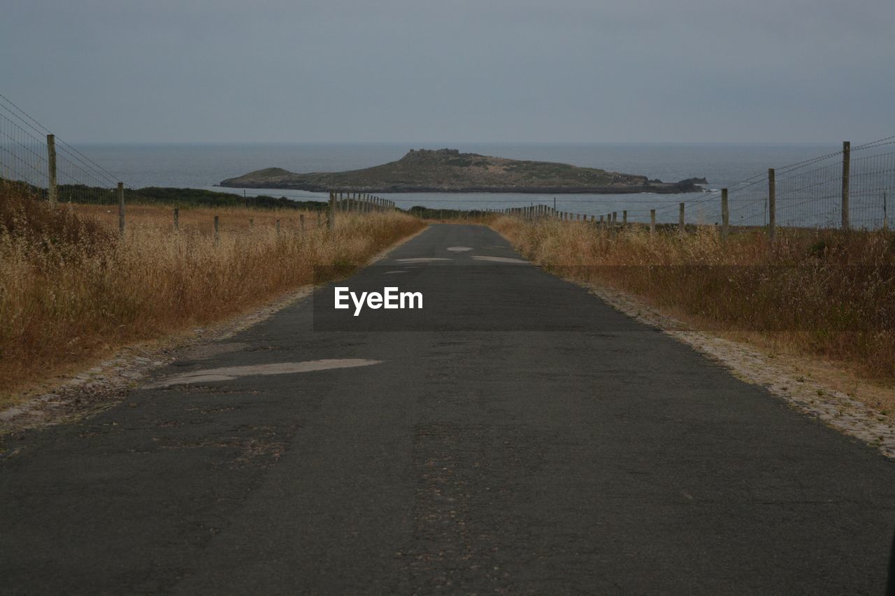 Empty road amidst field leading towards sea