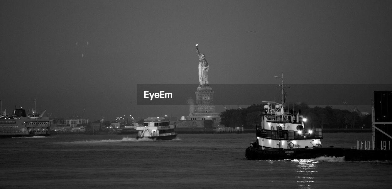 Trawlers sailing on sea by statue of liberty at night